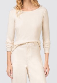 Beżowa dzianinowa bluzka z długim rękawem o szerokim dekolcie, gładkiej fakturze i dopasowanych rękawach, połączona z pasującymi beżowymi spodniami z wysokim stanem.