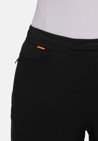 Black softshell pants with an elastic waistband, featuring a side pocket and a small orange accent on the waist, smooth texture.