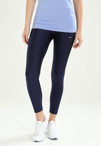 Marina leggings gjorda av stretchigt, slätt material, med en smal passform och ankellångt snitt, i kombination med vita träningsskor.