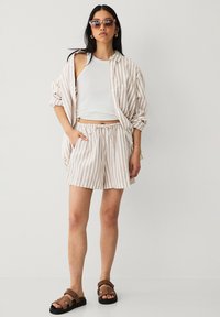 Beige og hvid stribet button-up skjorte, hvid tanktop, stribede shorts og brune sandaler. Glat stof og afslappet design.
