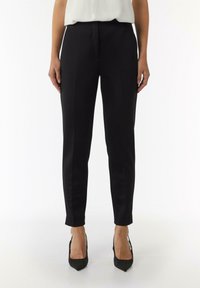 Schwarze maßgeschneiderte Hosen mit schlanker Passform, aus glattem Stoff, mit flacher Vorderseite und cropped Länge, kombiniert mit spitzen schwarzen Absätzen.