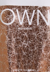 Texte "OWN WHO YOU ARE AND STAY DETERMINED" en grandes lettres blanches sur un fond marron avec un motif fissuré blanc.