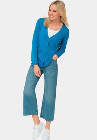 Blaues Strickjacke mit Knöpfen, V-Ausschnitt und langen Ärmeln, kombiniert mit weit geschnittenen Denim-Jeans und weißen Turnschuhen. Glatte Textur, lässiges Design.