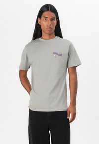 Gray cotton t-shirt with short sleeves, featuring a purple graphic design on the upper left chest area. Classic fit and minimal texture.