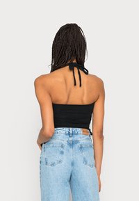 Top preto sem alças com as costas atadas, combinado com jeans de cintura alta azul claro. Textura suave, design ajustado e leve elasticidade.