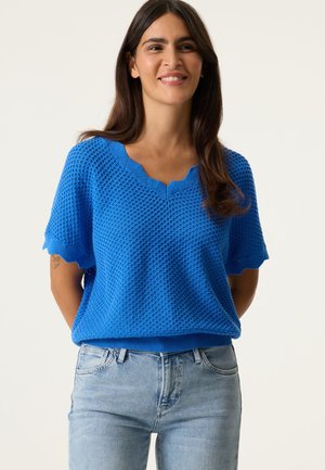 Pull bleu tricoté avec un motif texturé, encolure et bords de manches festonnés, associé à un jean ajusté bleu clair.