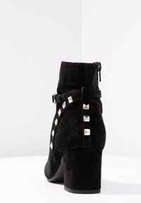 Stivale alla caviglia in suede nero con punta arrotondata, tacco a blocco di media altezza e dettagli in metallo argentato lungo il lato, con chiusura a zip.