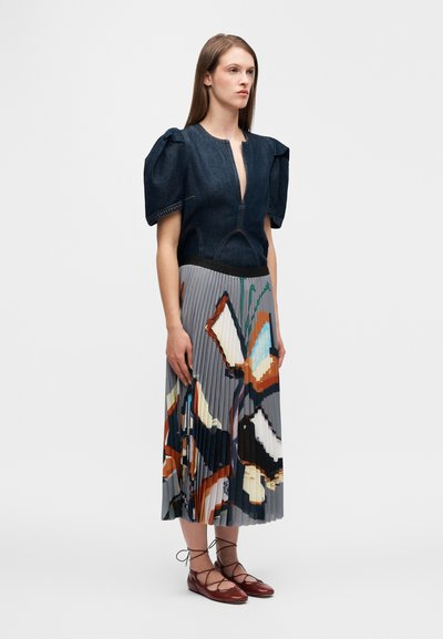 Haut en denim avec manches bouffantes et décolleté profond, associé à une jupe plissée présentant un motif abstrait coloré et une ceinture noire.