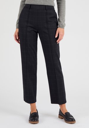 Pantalones de cuadros negros con corte ajustado, que presentan una parte delantera plana y un largo hasta los tobillos, combinados con mocasines de cuero negros.