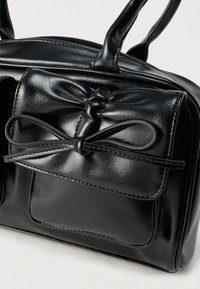 Czarna torebka z ekologicznej skóry z kokardą, dwoma uchwytami, zamkiem błyskawicznym i przednią kieszenią. Gładka faktura z kontrastowym przeszyciem.