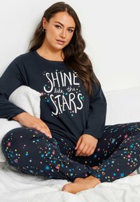 Marinblå pyjamas-set med långa ärmar som har en vit grafik "LYS som STJÄRNORNA" och färgglada stjärnmönster på byxorna. Mjukt material, avslappnad passform.