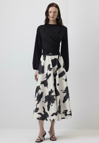 Black long-sleeve top with a wrap design paired with a flowing cream skirt featuring a bold black brushstroke pattern. Classic heeled sandals.