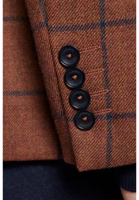 Brązowa marynarka w kratę z teksturowanego materiału, z czterema czarnymi guzikami na rękawie z pomarańczowymi akcentami.