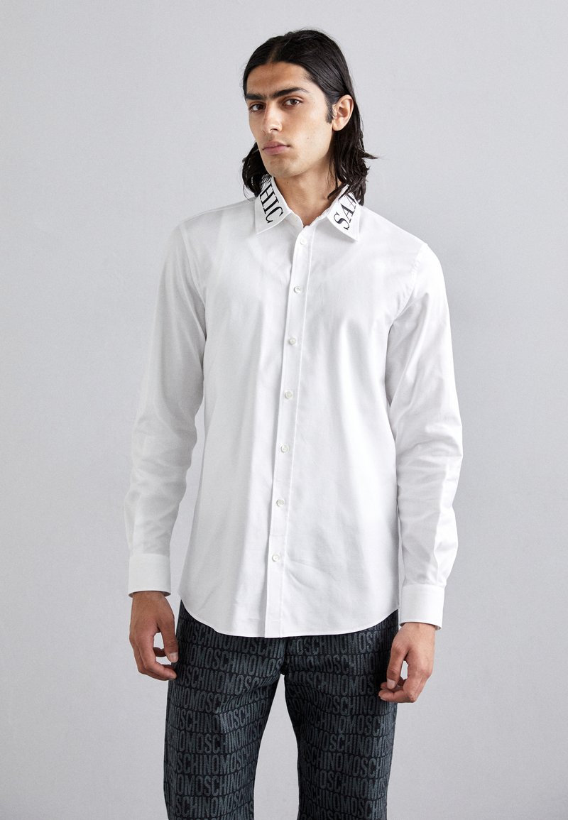 White button-up shirt with black embroidered text on collar, paired with black pants featuring a repeating logo pattern.