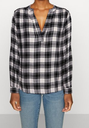 Chemise à manches longues à carreaux noir et blanc avec un col en V et des épaules froncées, fabriquée en tissu léger. Associée à un jean en denim bleu.