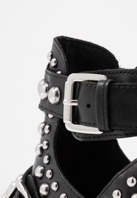 Czarne skórzane buty z srebrnymi ćwiekami i metalowym zapięciem. Design zawiera szeroki pasek z wycięciami. Gładka tekstura.