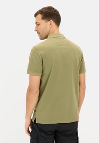 Oliven grøn polo t-shirt med korte ærmer, en klassisk krave og sideskår. Glat stof og en lille logo detalje nær kanten.