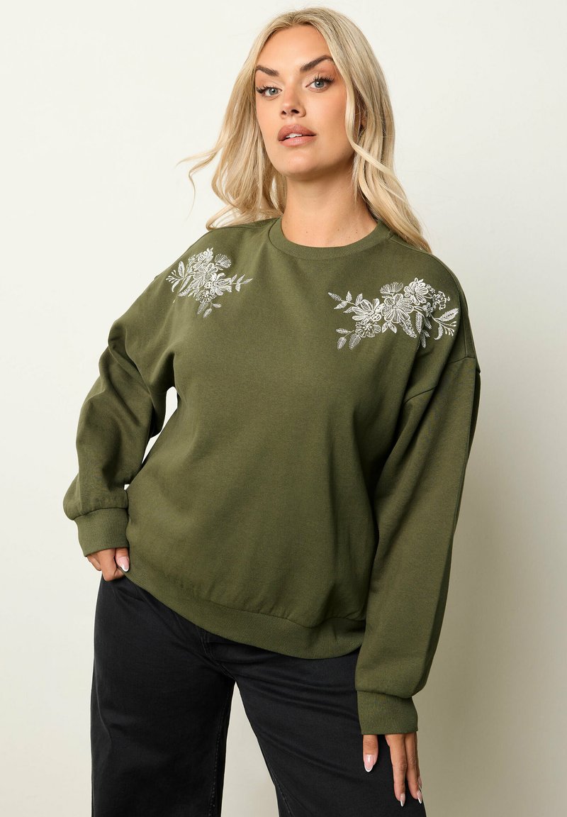 Sudadera verde oliva con bordado floral en los hombros, mangas largas y puños acanalados. Textura suave y ajuste relajado.