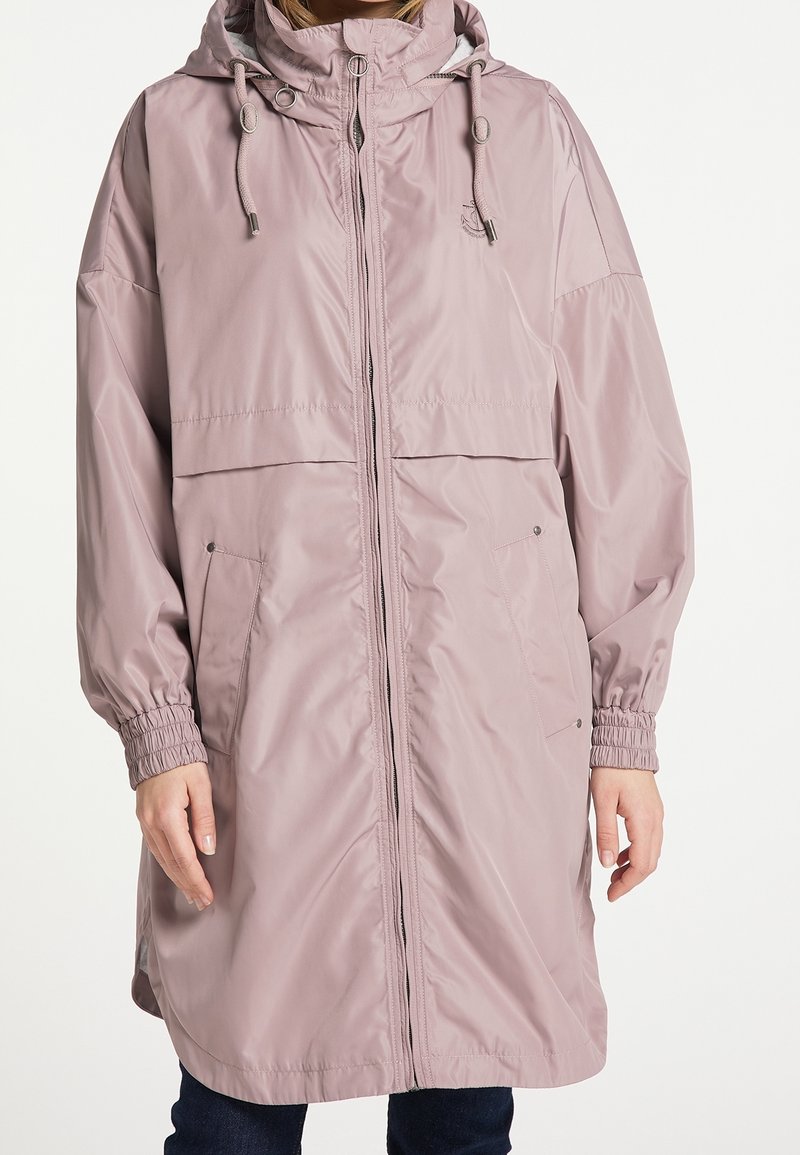 Imperméable mauve à capuche avec fermeture éclair à l'avant, capuche à cordon, poignets élastiques et poches latérales, porté par-dessus un pantalon foncé.