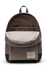 Zaino di tessuto grigio con copertura a pattina, accento arancione e interno a righe. Presenta una tasca frontale e un pannello inferiore nero.