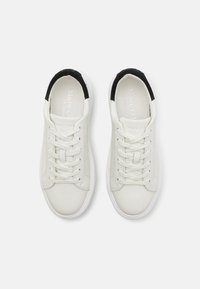 Sneaker in pelle bianca con design a collo basso, dettagli neri sul retro e lacci bianchi. Texture liscia e estetica minimalista.