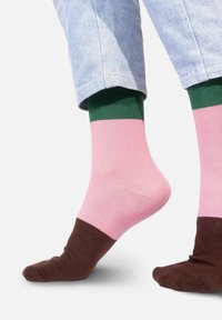 Kolorowe skarpetki z grubym splotem i wzorem zielonych, różowych i brązowych pasków. Górna część jest zielona, środkowa różowa, a palce brązowe.