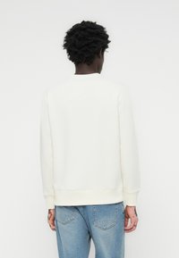 Witte sweatshirt met een ronde hals en lange mouwen. Kenmerkt zich door een effen textuur en geribbelde boorden aan de onderkant. Draagt gecombineerd met lichtblauwe jeans.