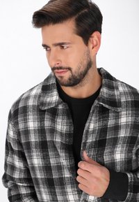 Czarna i biała koszula flanelowa w kratę z kołnierzykiem i zapięciem na guziki, charakteryzująca się miękką teksturą i długimi rękawami. Nosi się ją na czarnej bluzce.