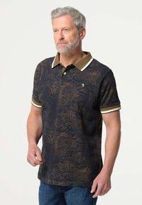 Zwarte polo met een gouden textuurpatroon, een bruine kraag en witte accenten op de mouwen. Voorzien van twee knopen en een geborduurd logo op de borst.