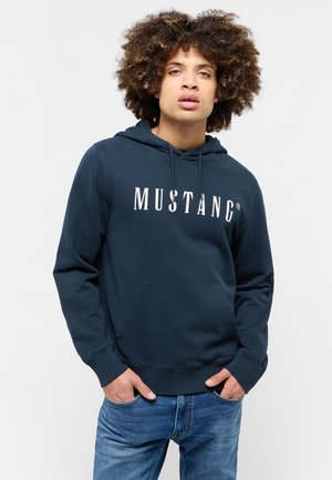 Námornícky modrá mikina s kapucňou obsahuje kangaroo vrecko, kapucňu so šnúrkou a biele logo "MUSTANG". Mäkká látka s rebrovanými manžetami a spodným lemom.