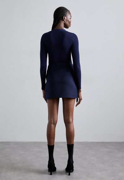 Knitted navy bodysuit with long sleeves, paired with a fitted mini skirt. Chunky ribbed texture, accentuated by sleek high heels and socks.
