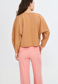 Brązowy top z szerokimi rękawami i okrągłym dekoltem, w połączeniu z różowymi, dopasowanymi spodniami z kieszeniami i gładką teksturą materiału.