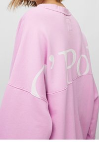 Sudadera rosa con corte relajado, que presenta texto blanco en la parte posterior. Fabricada con un material suave con acabado texturizado y cuello acanalado.