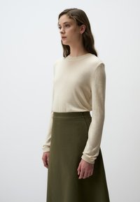 Maglioncino crema con maniche lunghe e collo rotondo, abbinato a una gonna verde oliva a vita alta, in tessuto liscio e con un design minimalista.