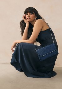 Navy, floor-length dress in smooth fabric, paired with a textured navy clutch with silver hardware, featuring a folded design and chain strap.