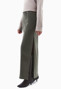 Khakigrøn denimskirt med høj slids, med lynlås lukning og skrå syning, parret med sorte spidse støvler.