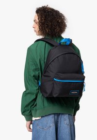 Zaino nero con dettagli blu, realizzato in tessuto resistente, dotato di una tasca frontale, spallacci regolabili e un design arrotondato.