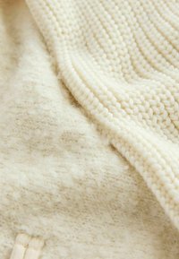 Cream-colored knitted fabric with a textured, fluffy surface; features a ribbed pattern and smooth sections. Soft and lightweight material.