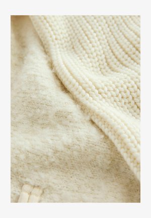 Cremfarbener Strickstoff mit einer strukturierten, flauschigen Oberfläche; weist ein Rippmuster und glatte Abschnitte auf. Weiches und leichtes Material.