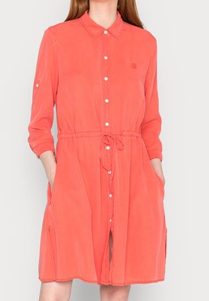 Koralfarvet kjole med knapper, krave, snøre i taljen, lange ærmer og sidelommer. Blødt stof med en glat tekstur.