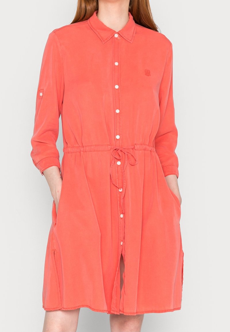 Robe-chemise corail avec col, taille à cordon, manches longues et poches latérales. Tissu doux avec une texture lisse.