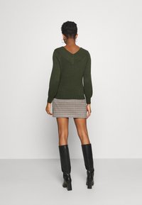 Dark green knit sweater with a V-neck back, paired with a patterned mini skirt in shades of brown and cream. Black knee-high boots.