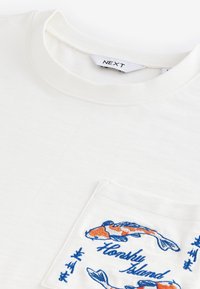 White cotton t-shirt featuring a chest pocket with blue and orange koi fish embroidery and "Honshu Island" text. Round neck design.