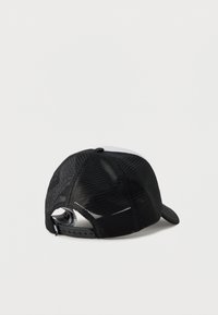 Μαύρο τρακέρ καπέλο με πλέξη, εμφανίζεται από πίσω με ρυθμιζόμενο κούμπωμα τύπου snap και ορατές εσωτερικές ετικέτες, σε απλό φωτεινό φόντο.