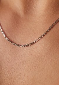 Zilveren ketting met verlengde schakels die op de huid rusten, en een gladde textuur tonen met een close-up van de metalen glans.