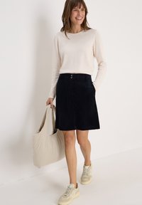 Jupe en velours côtelé marine avec une coupe droite, dotée de deux poches et de deux boutons à la taille, associée à un pull beige clair et des baskets.