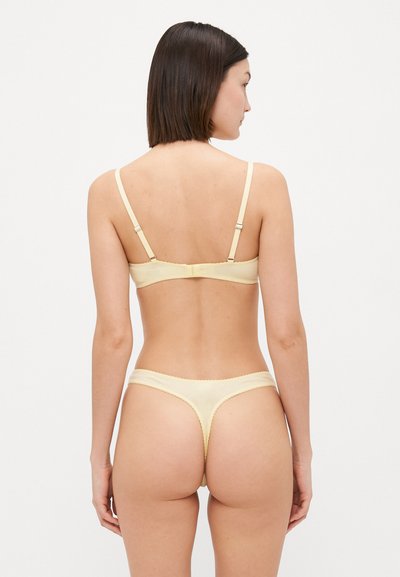 Kollane pesu komplekt, mis sisaldab braletti ja stringe. Pehme kangas, laineliste äärte ja reguleeritavate rihmadega, millel on lihtne disain.