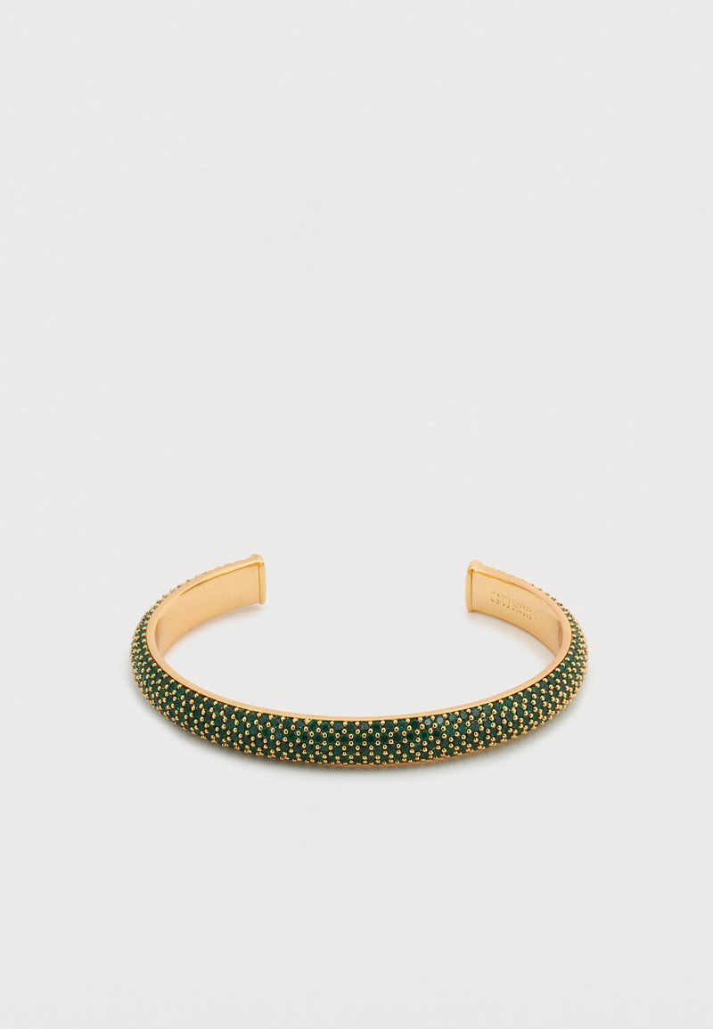 Το πράσινο βραχιόλι με μανσέτα διαθέτει ομαλή μεταλλική επιφάνεια με χρυσές λεπτομέρειες και υφή κατά μήκος της ταινίας, αναδεικνύοντας μικρά, ανάγλυφα στοιχεία.