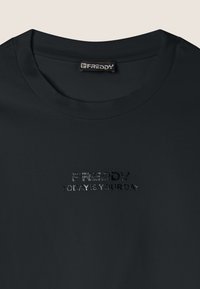 T-shirt nera a maniche corte in tessuto morbido, con un design in rilievo stampato che recita "FREDDY OGGI È IL TUO GIORNO" sulla parte anteriore.