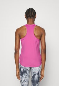 Top atletico aderente senza maniche in tessuto rosa brillante, con design a schiena scoperta e morbida texture, abbinato a leggings a fantasia.